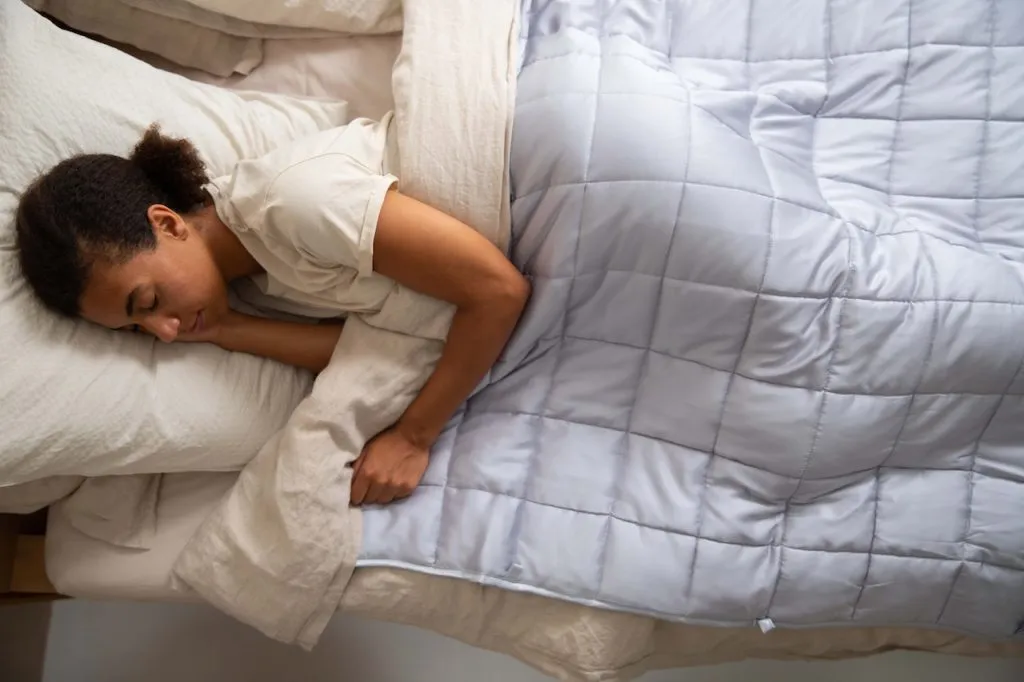 Holistic Health Tips 2 A woman practicing holistic health tips by making she she gets quality sleep time in a comfortable bed with a blanket.