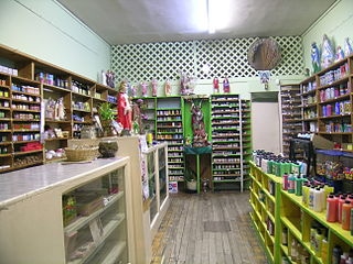 A small, brightly lit store with shelves filled with various colorful candles and spiritual items. The wooden floor and green accents create a cozy atmosphere.
