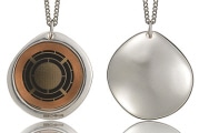 Two metallic pendant necklaces. One pendant features a circular design with a grid pattern, while the other has a smooth, plain surface. Both pendants are on silver chains.