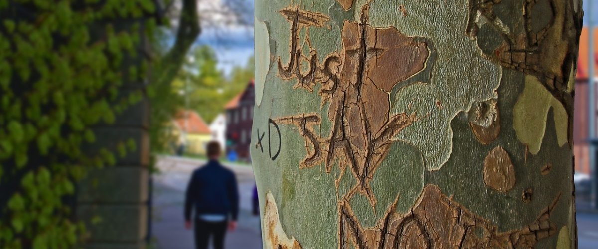 A person setting healthy boundaries while walking down the street next to a tree with graffiti on it.