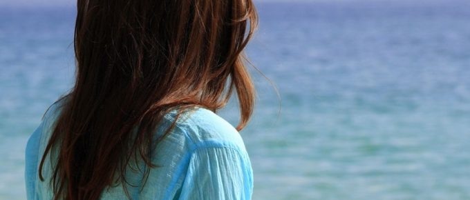 A woman wearing a blue shirt looking at the ocean, reflecting on past experiences.