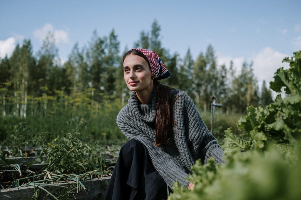 A woman practicing holistic health tips while kneeling down in a vegetable garden.
