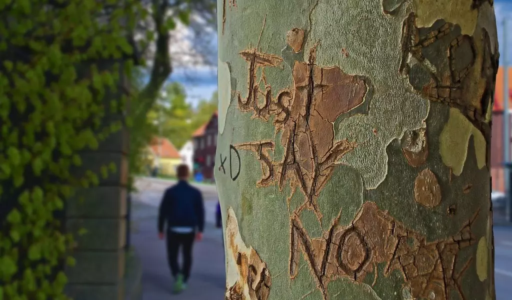 A person setting healthy boundaries while walking down the street next to a tree with graffiti on it.