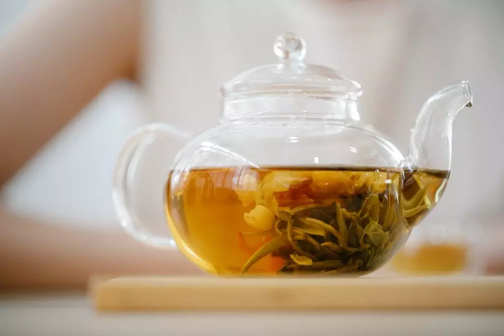 A holistic health tip: Glass teapot with green tea on a wooden table.
