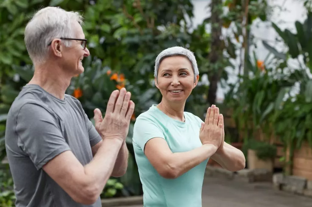 An older couple practicing holistic health by doing yoga in a garden.