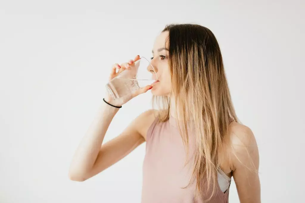 A young woman practicing holistic health by drinking water from a glass.