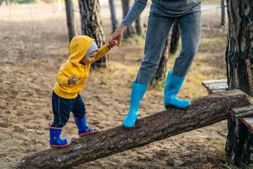 A mother and child are engaging in holistic health practices by standing on a log in a park.