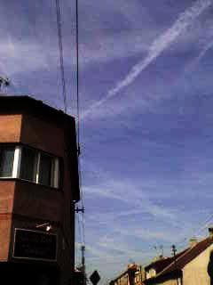 Building corner with a large window on the left, power lines extend upwards, and a clear sky with light clouds above.
